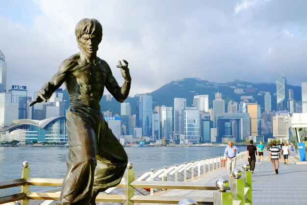 Foto persone che camminano vicino alla statua di bruce lee a tsim sha tsui contro un cielo nuvoloso