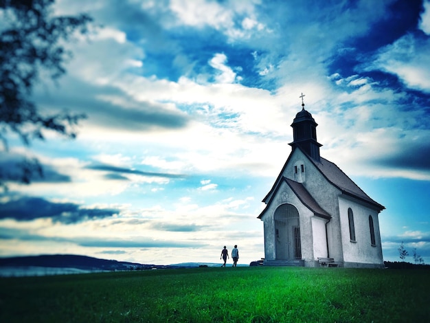 people walking by chapel against cloudy sky