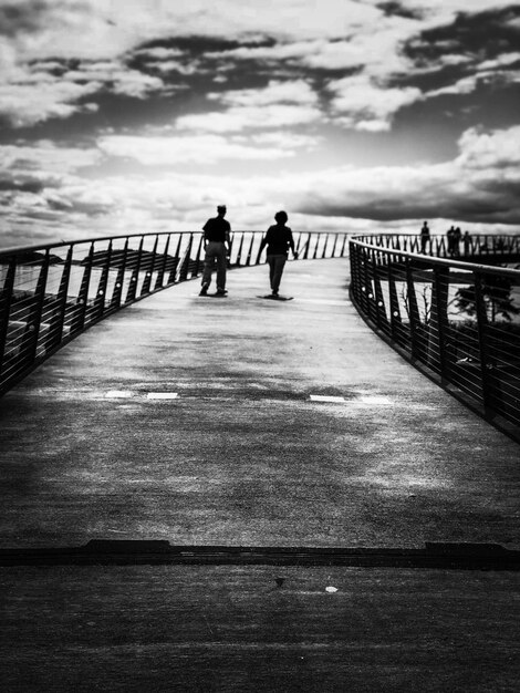 People walking on footbridge against sky