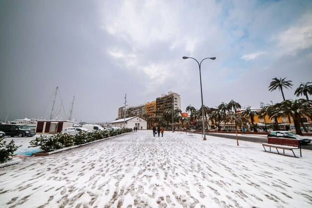 スペインの町デニアの雪に覆われた港を歩く人