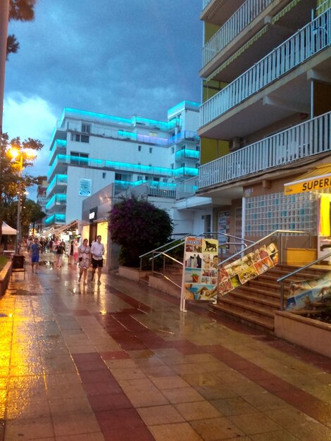 People walking on street amidst buildings in city against sky