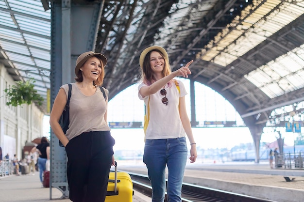 People walking with suitcase at the railway station. Happy mother and teenager daughter traveling with luggage together. Transport, tourism, moving, family concept