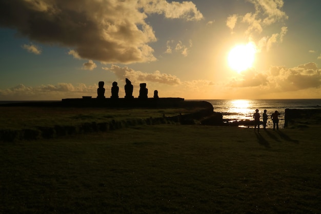 Люди смотрят закат над Тихим океаном в Аху Тахай со статуями Моаи, остров Пасхи, Чили