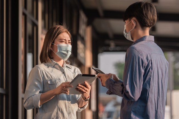 Le persone indossano una maschera facciale per proteggere il coronavirus parlando di affari con la tecnologia tablet
