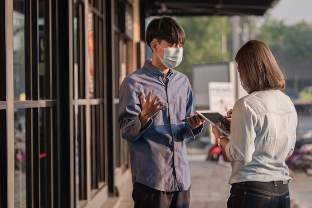 사람들은 안면 마스크를 착용하여 태블릿 기술로 코로나 바이러스 말하는 비즈니스를 보호합니다.