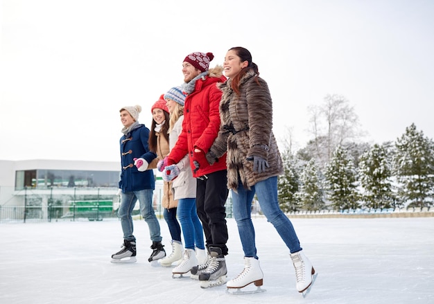 Фото Люди, зима, дружба, спорт и концепция отдыха - счастливые друзья катаются на коньках на катке на открытом воздухе