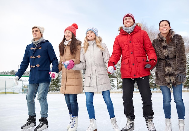 Concetto di persone, inverno, amicizia, sport e tempo libero - amici felici che pattinano sul ghiaccio sulla pista di pattinaggio all'aperto