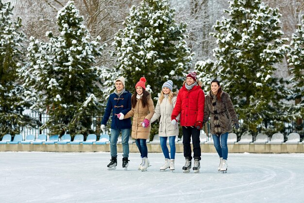 People, winter, friendship, sport and leisure concept - happy\
friends ice skating on rink outdoors