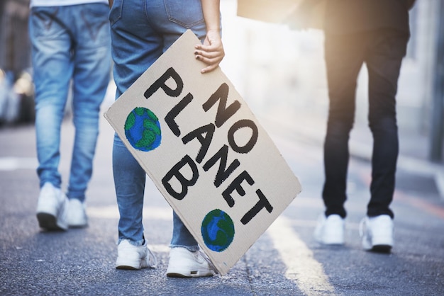 Foto persone con poster o striscioni sul cambiamento climatico protestano su strada asfaltata o in città le gambe di un gruppo di donne camminano o si radunano per il riscaldamento globale, il cambiamento dell'ambiente mondiale o salva il pianeta con il bagliore