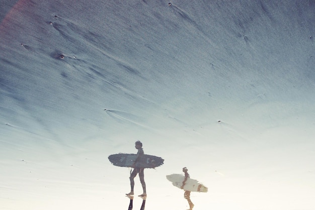 Foto persone con una tavola da surf riflessa sulla spiaggia bagnata