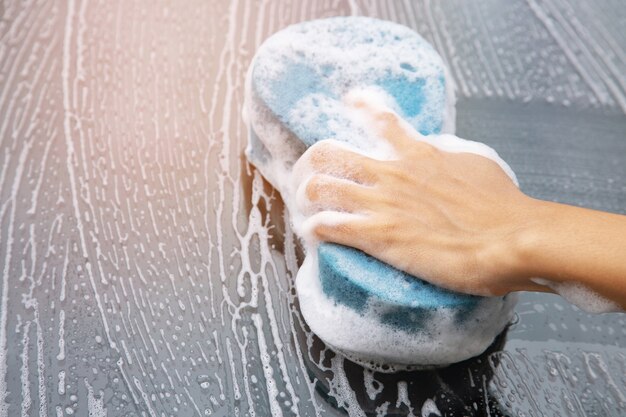 People worker man holding hand blue sponge and bubble foam cleanser window for washing car.