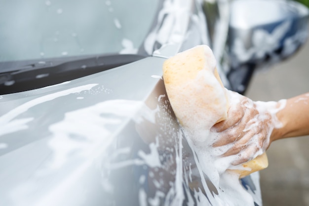 車を洗うための黄色いスポンジと泡泡クレンザーウィンドウを手に持っている人々の労働者の男。コンセプトカーウォッシュクリーン。メッセージを書き込むためのスペースを残します。