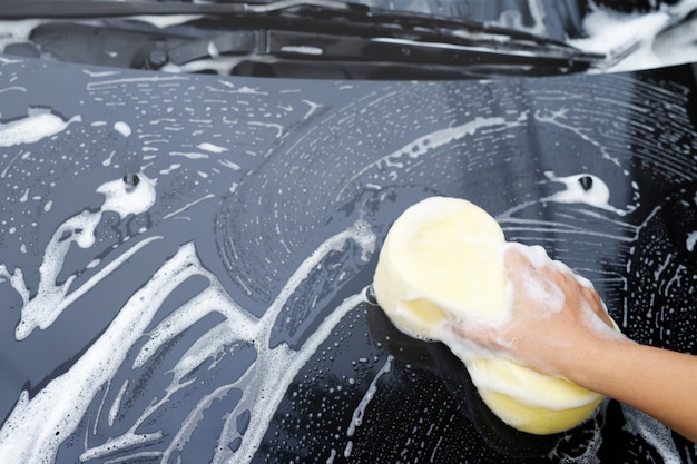 Persone lavoratore uomo che tiene la mano spugna gialla e finestra detergente schiuma a bolle per il lavaggio auto. concetto di autolavaggio pulito. lascia spazio per scrivere messaggi.