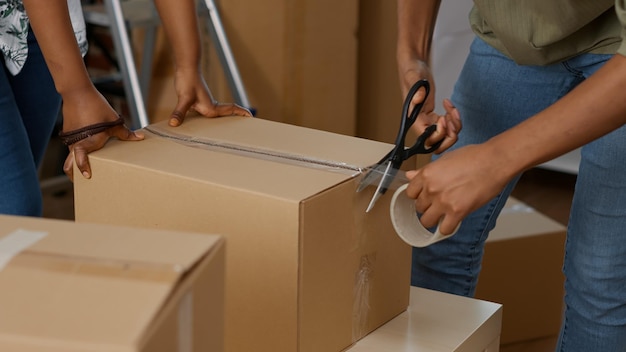 人々は、粘着テープローラーで段ボール箱を包み、移転のために輸送するために家具を梱包します。ローンで購入した新しい家のカートンパッケージコンテナに接着剤スコッチを使用。閉じる。