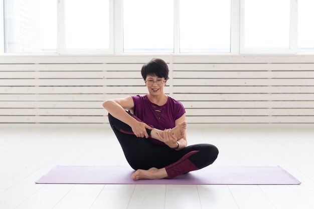 People, yoga, sport and healthcare concept - Attractive middle-aged woman stretching and sitting in