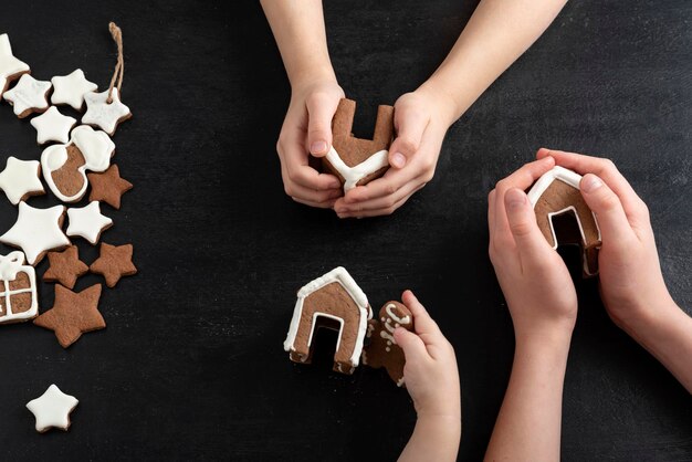 Peperkoekhuizen en sterrenkoekjes in kinderhanden. Zwarte achtergrond, bovenaanzicht.