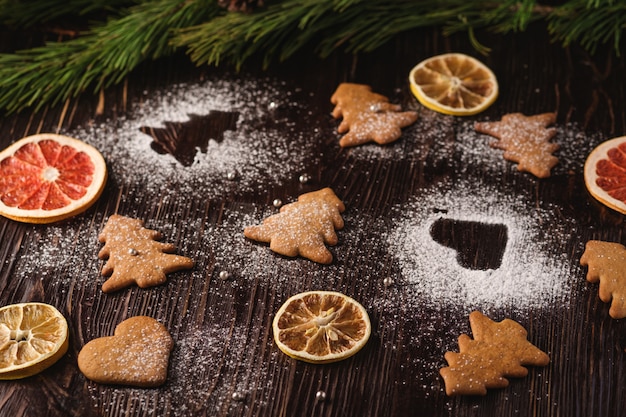 Peperkoekkoekjes in Kerstboom en hartvorm, poedersuiker op houten tafel, citrus gedroogd fruit, sparrentak, hoekmening, selectieve aandacht