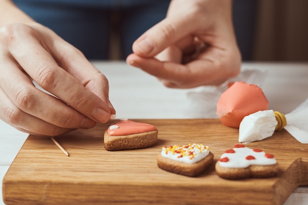 Foto peperkoekkoekjes versieren met suikerglazuur. de vrouwenhanden verfraaien koekjes in vorm van hart, close-up