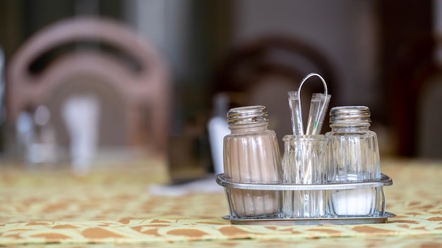 Peperstrooiers en zoutvaatjes een servettenstandaard staan op tafel in een café De tafel in het restaurant is bedekt met een tafelkleed Witte papieren servetten op een standaard en een glazen bak met suiker