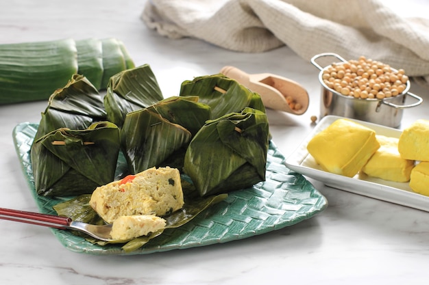 Пепес Таху - индонезийский пряный тофу, завернутый в банановый лист и приготовленный на пару, типично индонезийская еда с Западной Явы (суданский язык). Тофу на пару с азиатским базиликом, белый фон