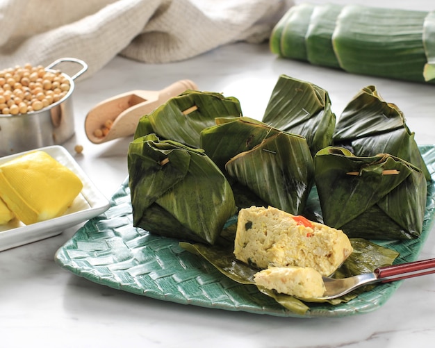 Pepes tahu è il tofu speziato indonesiano avvolto con foglie di banana e cotto a vapore, cibo tipicamente indonesiano di giava occidentale (sudanese). tofu al vapore con basilico asiatico, sfondo bianco