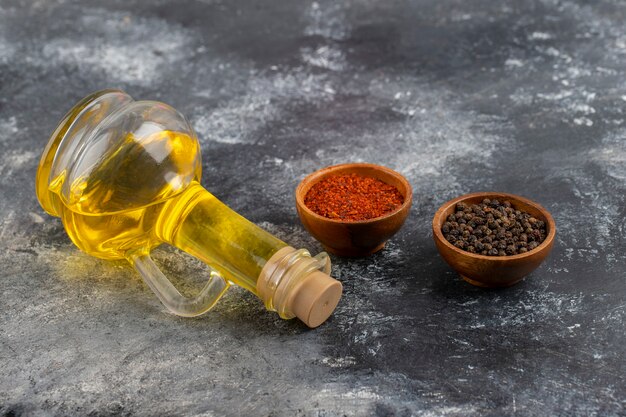 Pepper corns with powder and a glass bottle of oil placed on stone table. 