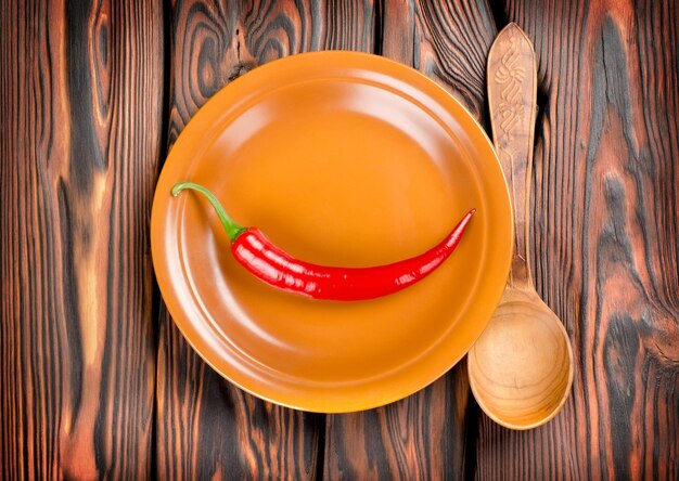 Перец в тарелке и ложке на деревянном фоне