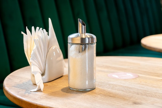 Pepper shakers and salt shakers a napkin stand are on the table in a cafe The table in the restaurant is covered with a tablecloth White paper napkins on a stand and a glass container with sugar