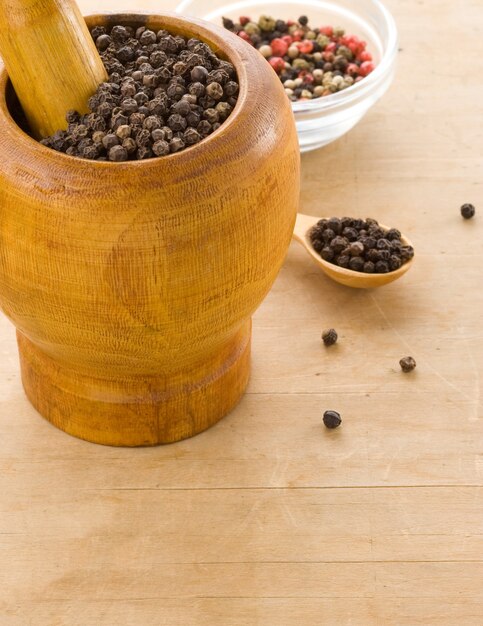 Pepper spices and mortar with pestle on wooden texture