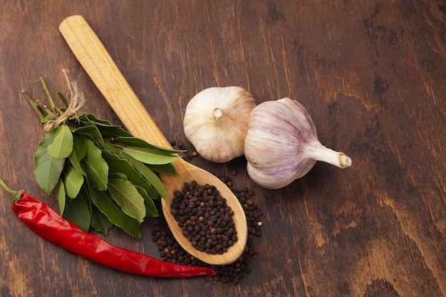 Pepper in wooden spoon with garlic bay leaves and chili pepper Spices