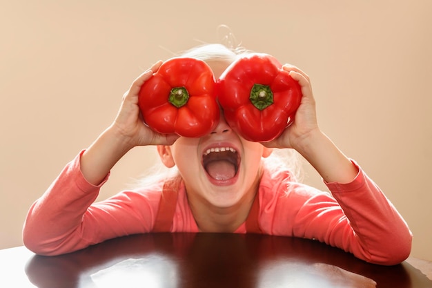 Peppercheerful child has fun holding pepper in front of her eyes as if in glasses with open mouth