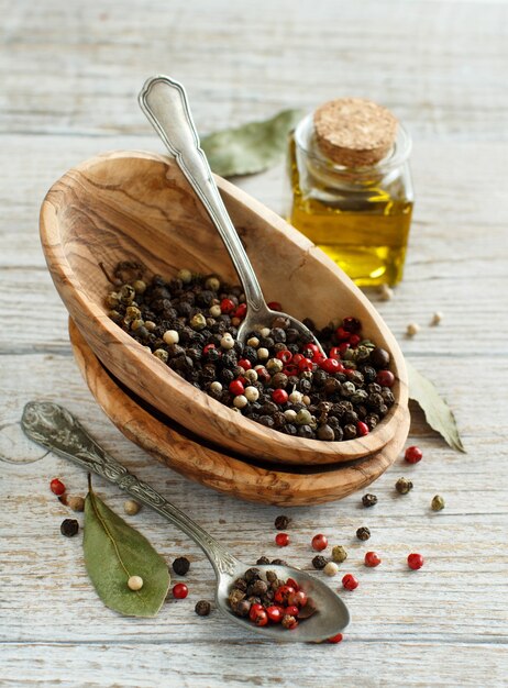 Peppercorn mix in a bowl, bay leaves and olive oil on a wooden table