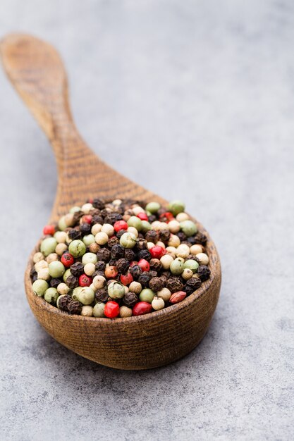 Peppercorn mix in a wooden bowl on grey table.