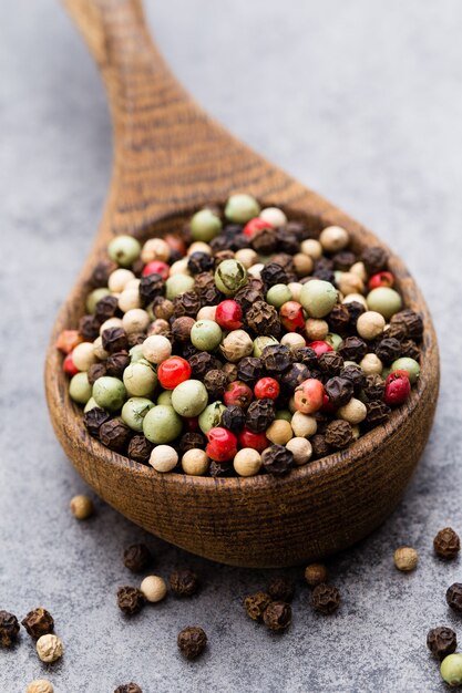 Peppercorn mix in a wooden bowl on grey table.