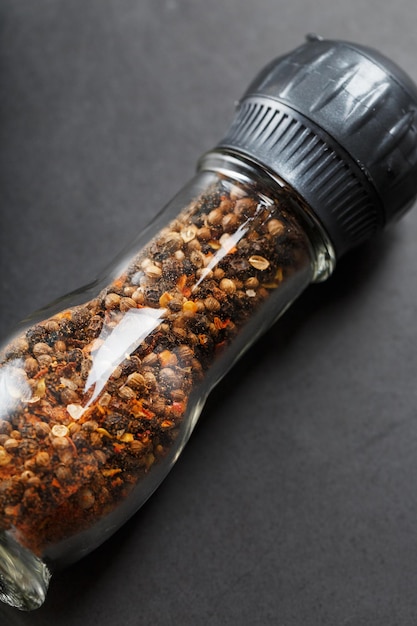 Peppercorns cumin and salt in a transparent mill on a black background