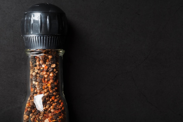 Peppercorns cumin and salt in a transparent mill on a black background