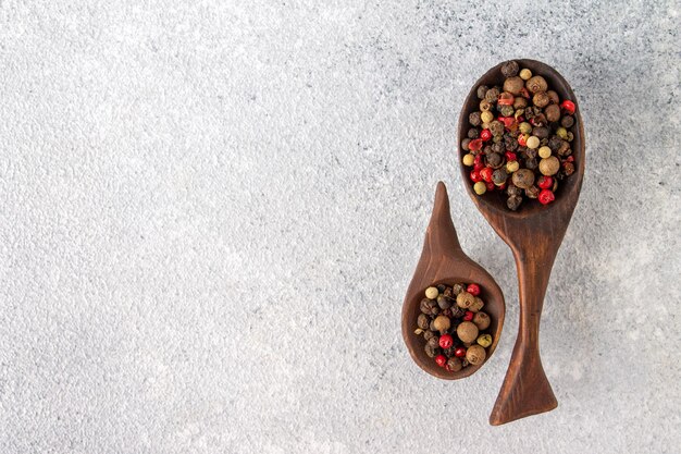 Peppercorns lie in wooden spoons copy space