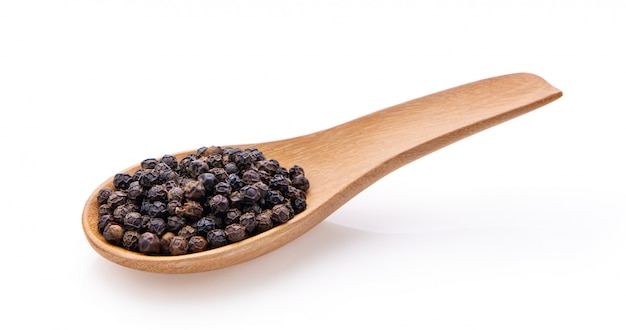 Peppercorns in wood spoon on white wall