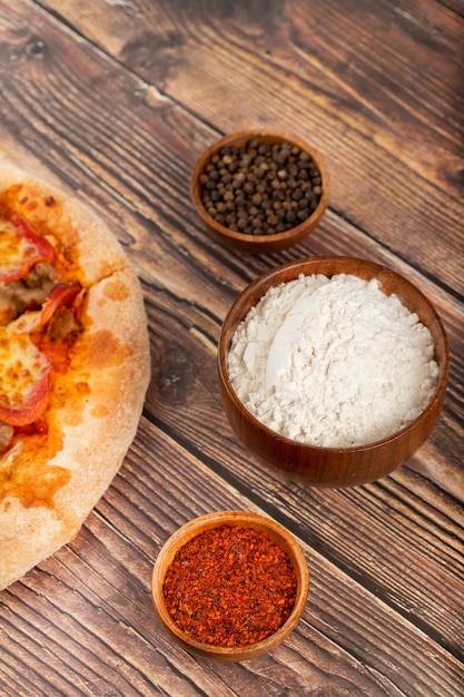 Pepperoni pizza, bowl of flour and spices on wooden table. 