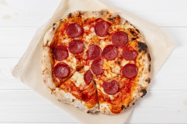 Pepperoni pizza in a box on a white wooden table