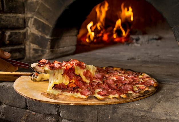 pepperoni pizza cheese pull in front of wood oven with fire in background