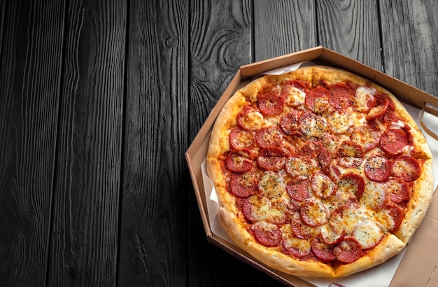 Pepperoni pizza on dark black wooden board, top view, place for text, traditional italian pizza