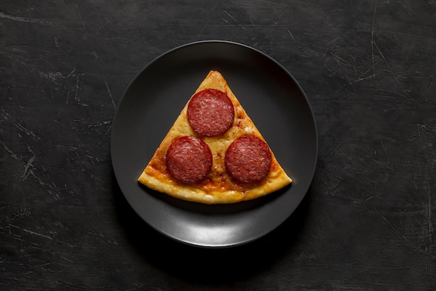 Pepperoni pizza een driehoekig stuk op een grijze ronde plaat op een donkere achtergrond bovenaanzicht ruimte om tekst te kopiëren