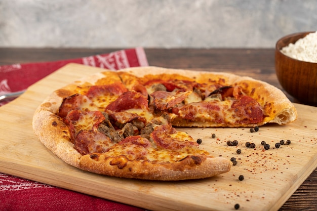 Pepperoni pizza slices on wooden cutting board with flour. 