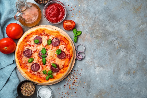 Pepperoni pizza, tomatoes, tomato sauce, onions, olive oil and spices on a gray background. The concept of cooking, fresh baking.