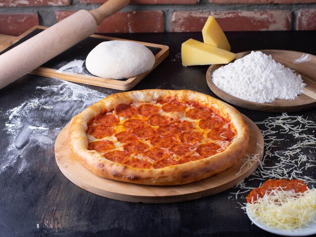 Pepperoni Pizza - Verse zelfgemaakte pizza met pepperoni, kaas en tomatensaus op rustieke houten achtergrond met ingrediënten