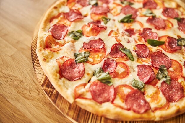 Pepperoni pizza with salami, cheese, tomatoes and basil on wooden table