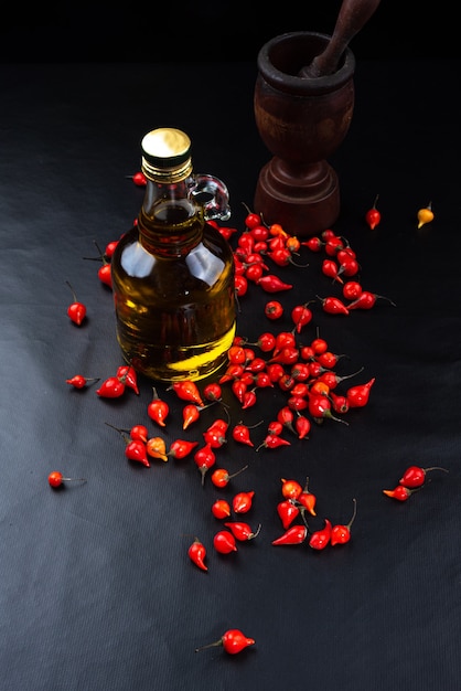 Peppers, olive oil and wooden mortar on black background top view