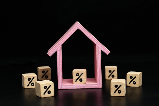 значок символа процента на деревянном блоке и деревянный дом на темном фоне