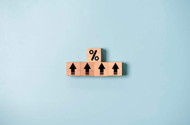 Percentageteken en pijl-omhoog op houten kubusblok en blauwe achtergrond voor verhoging van de financiële rente en groei van bedrijfsinvesteringen vanuit dividendconcept
